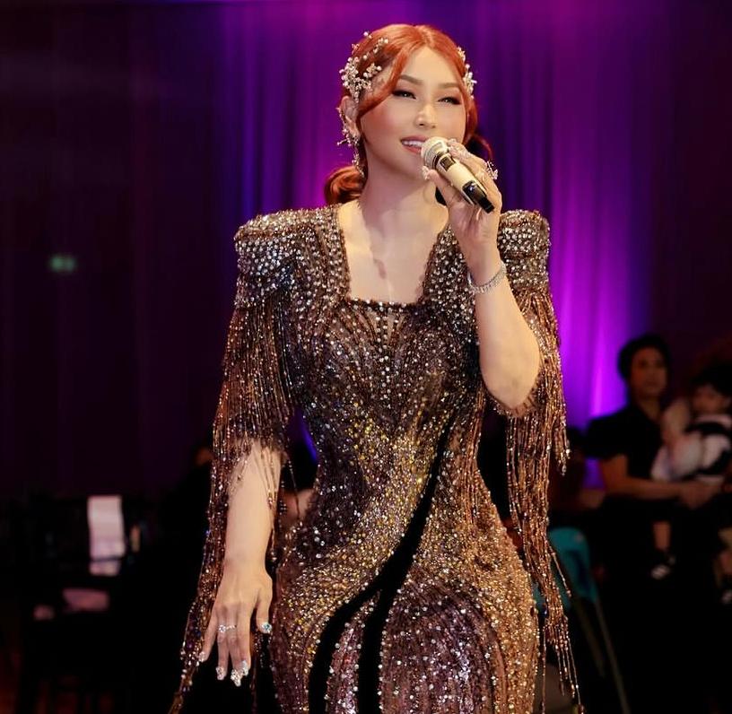 Whatsapp image 20260621 at 11 07 39 catrawarta Female singer on stage wearing a glittering gold sequined gown holding a microphone